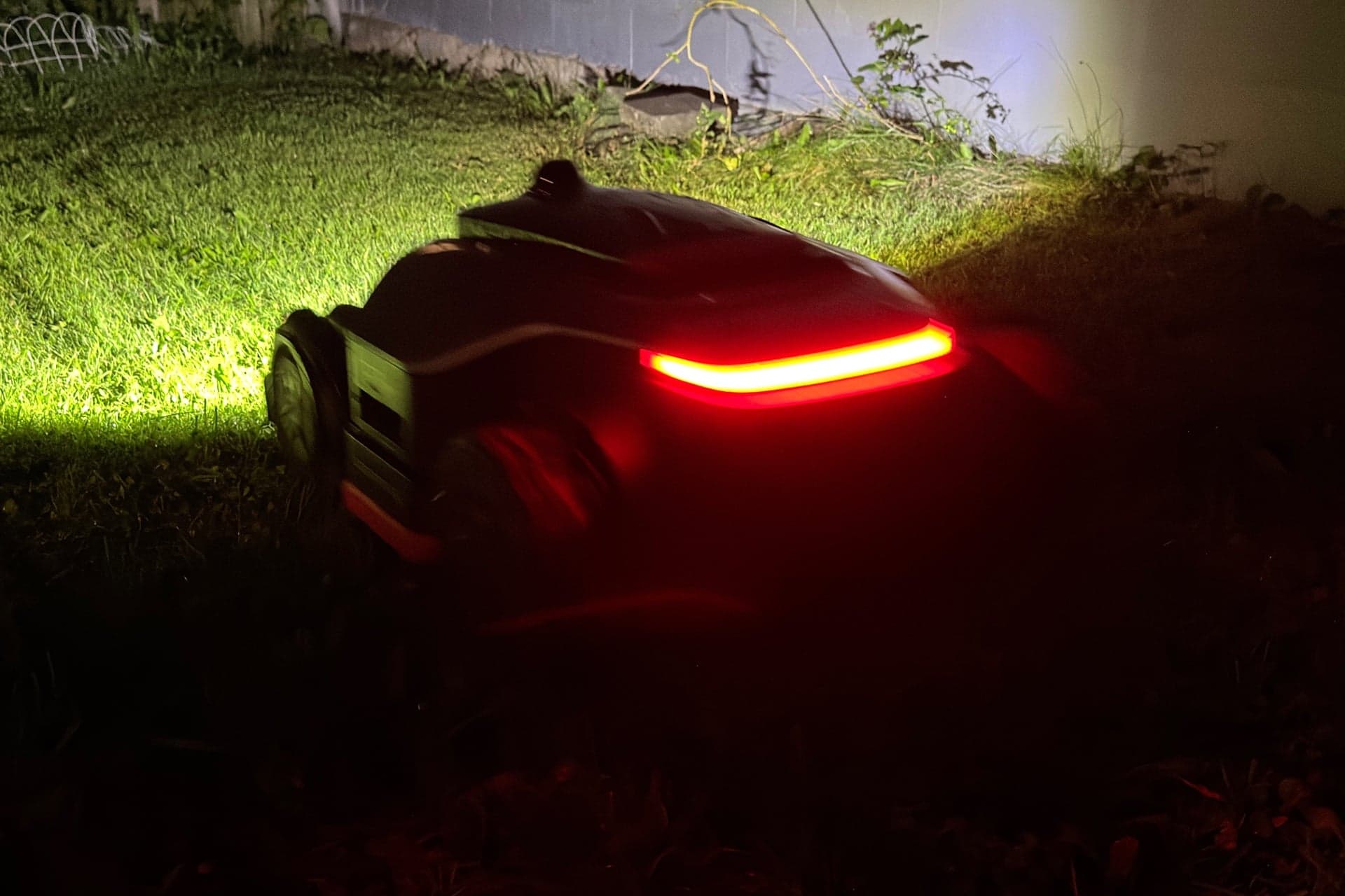 Dreame A3 AWD Pro 3500 mowing at night, with its rear red LED strip and front headlight visible — © Wes Davis / Gizmodo