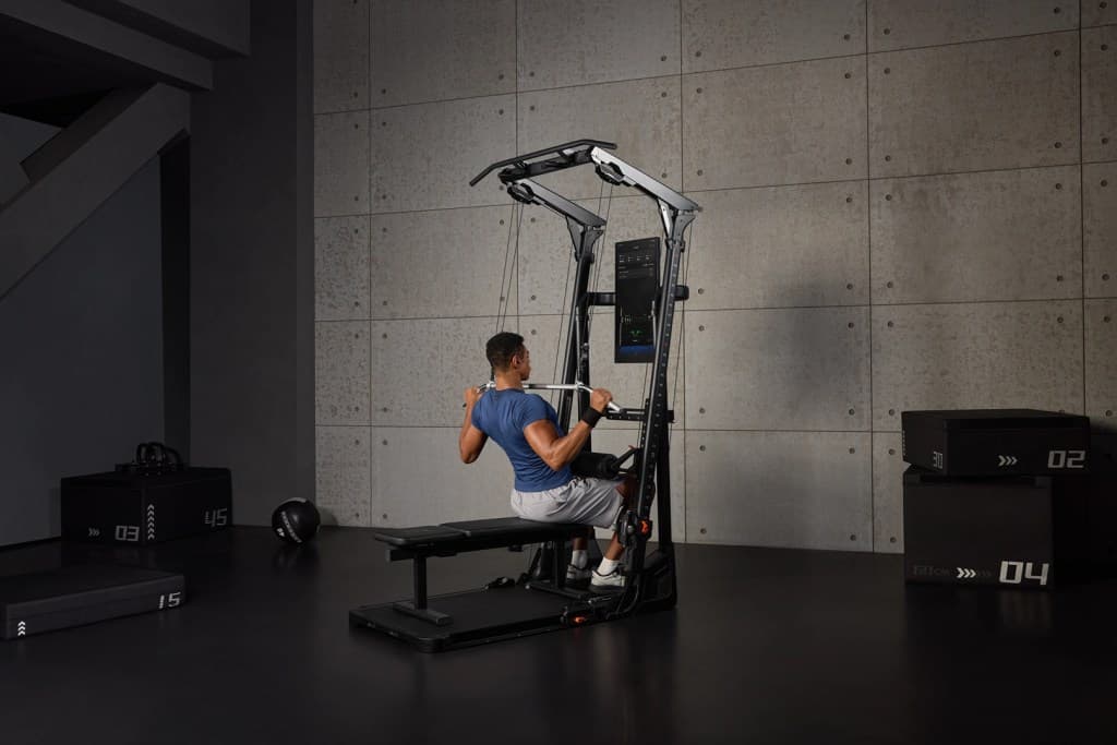A person performing a seated exercise on a versatile gym equipment, focusing on strength training in a modern gym setting with concrete walls.